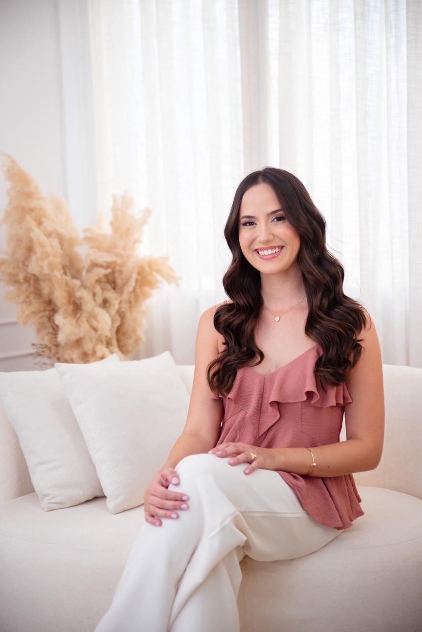 Dra. Laura Uchôa sorrindo, sentada em sofá em ambiente acolhedor